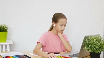 Serious schoolgirl sitting at table with laptop and textbook and doing homework. Study from home video