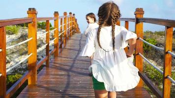 Back view family mother and daughters walking on wooden deck near the beach enjoying tropical summer vacation. video