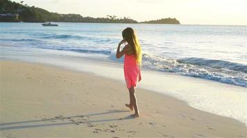 adorabile contento poco ragazza hvaing divertimento su bianca spiaggia a tramonto. lento movimento video