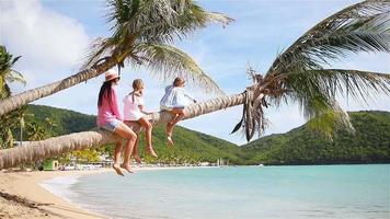 Mother and two kids having fun on white beach. Family sitting on the palm tree