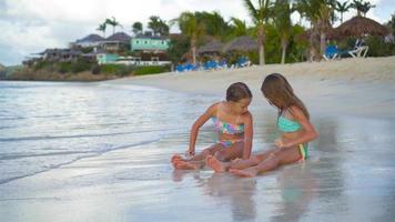 Adorable little girls playing with sand on the beach. Kids sitting in shallow water and making a sand castle video