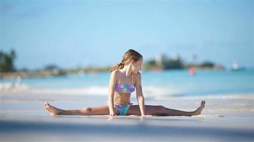 Adorable active little girl is sitting on a twine on a snow-white sandy beach video