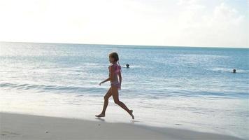 pequeño activo niña haciendo volteretas en el playa a atardecer.lento movimiento video