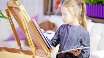 Adorable little girl painting a picture on easel indoor video