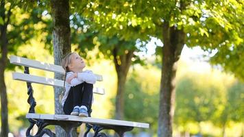 adorable pequeño niña a hermosa otoño día al aire libre. linda niño sentado en el banco en al aire libre parque en otoño video