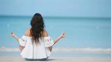 linda garota em posição de ioga durante as férias tropicais. mulher jovem e saudável sentada em posição de ioga meditando na praia video