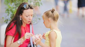 giovane madre e sua figlie mangiare ghiaccio crema all'aperto. mamma feed il suo figlia gelato nel il strada video