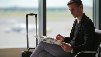 jovem caucasiano com jornal no aeroporto enquanto aguardava o embarque. casual jovem empresário vestindo paletó. video