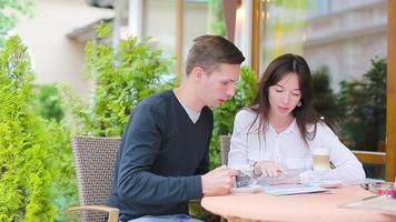 Restaurant tourists couple with coffee and map at outdoor cafe. Young woman and man enjoy time outside ay warm summer day video
