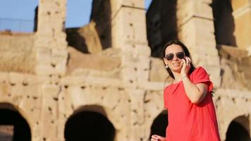 Happy caucasian girl talks by cell phone in front of most popular destination in the world Colosseum in Rome, Italy. Girl enjpy her italian vacation video