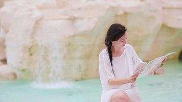 hermosa mujer mirando el mapa turístico de la ciudad cerca de la fuente de trevi, roma, italia. niña feliz disfruta de vacaciones italianas en europa. video