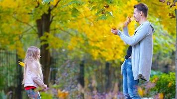 adorable pequeño niña y contento padre disfrutar otoño día en otoño parque al aire libre. otoño familia vacaciones video