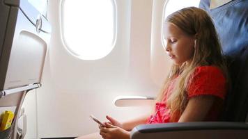 Adorable little girl traveling by plane sitting near window. Kid listening music sitting near aircraft window video