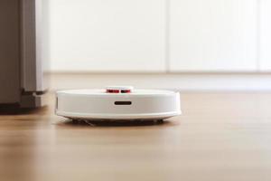 white robot vacuum cleaner cleans the floor from debris,home cleaning with an electric vacuum cleaner,vacuum cleaner electric robot cleaning technology,top view of a robot vacuum cleaner.