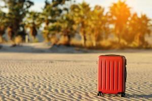 Summer travel and tourist planning vacation. Red suitcase in the beautiful sand beach on palms trees and sunlights background. Early booking for summer holidays. Place for text photo