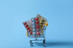 Shopping cart filled with pills. Blue background. Concept full set of medicines in the store. photo