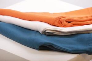 Pile of knitted warm colorfull sweaters with different knitting patterns folded in stack on white background, white wall background. Fall winter season knitwear. Close up, copy space for text photo