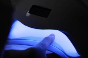 Closeup view of female hands with gel polish manicure. Woman puts hand into led uv lamp for curing top cover of nailpolish. UV lamp, LED Nail photo