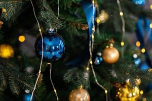 Fir tree decorated with christmas gold and blue balls. Close-up of beautiful christmas tree with illuminated garland and blue ribbons. Merry Xmas and Happy Holidays greeting card, New Year. Noel. photo