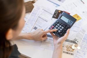 cerca arriba mano de estrés asiático joven mujer de negocios utilizando calculadora para calcular impuesto, gastos de facturas, crédito tarjeta para pago en debido fecha límite en mesa a hogar. financiero, Finanzas personas concepto. foto