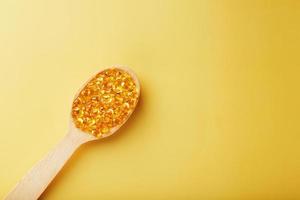 Vitamin D3 Capsules in a spoon with other vitamin D3 capsules around them on a yellow background photo