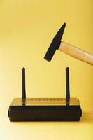 A hammer hits the Wi-Fi modem router to break it against a yellow background. photo