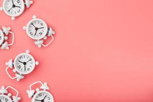 A pattern of many white classic alarm clocks in the form of a pattern on a pink background. Top view with a copy of the space, flat lay. photo