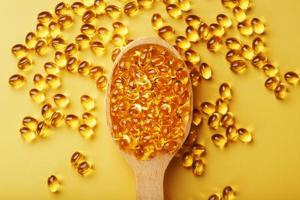 Vitamin D3 Capsules in a spoon with other vitamin D3 capsules around them on a yellow background photo