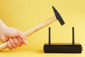 A hammer hits the Wi-Fi modem router to break it against a yellow background. photo
