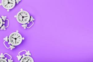 A pattern of many white classic alarm clocks in the form of a pattern on a purple background. Top view with a copy of the space, flat lay. photo