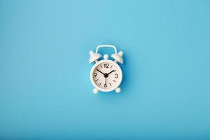 White retro alarm clock on blue background. Concept of time with free space for text. photo