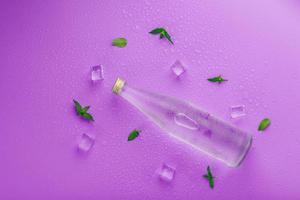 A bottle with an ice drink in drops of condensation, ice cubes and mint leaves on a pink background photo