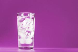 vaso con agua y cubitos de hielo sobre un fondo rosa foto
