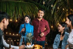 Portrait of Happy Asian friends having dinner party together - Young people sitting at bar table toasting beer glasses dinner outdoor  - People, food, drink lifestyle, new year celebration concept. photo