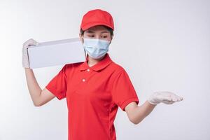 Image of a conscious young delivery man in red cap blank t-shirt uniform face mask gloves standing with empty white cardboard box isolated on light gray background studio photo