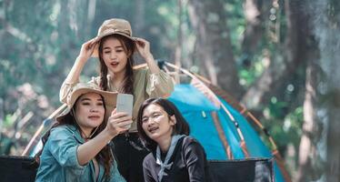 Asian pretty woman and girlfriend use smartphone selfie on camping photo