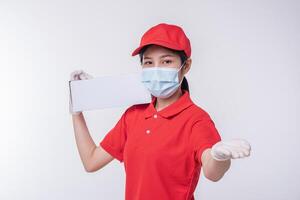 Image of a conscious young delivery man in red cap blank t-shirt uniform face mask gloves standing with empty white cardboard box isolated on light gray background studio photo