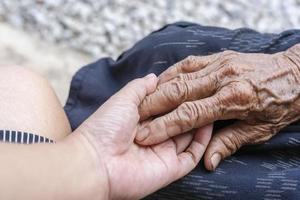 Close-up of old and young holding hands. Middle-aged mommy's wrinkled hands holding young daughters, a millennial woman supporting mature mum, showing care, and love. Support for the elderly concept. photo