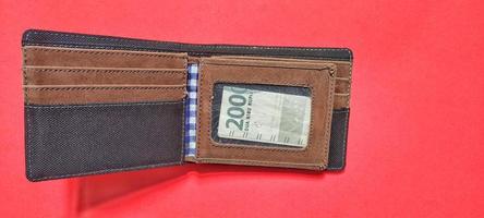 Top view of A brown wallet containing Indonesian banknotes worth 2,000 rupiah isolated on a red background. photo