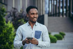 joven contento africano americano masculino persona de libre dedicación correspondiente en móvil y leyendo bueno Noticias foto