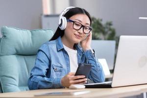 vídeo charla con amigos.jovenes asiático mujer vistiendo auriculares,sosteniendo un teléfono hablando en vídeo llamada foto