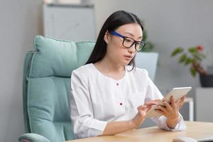 Online admission to the hospital. A young beautiful Asian woman doctor with tablet photo