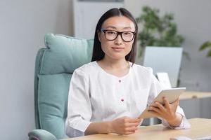 Online admission to the hospital. A young beautiful Asian woman doctor with tablet photo