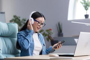 vídeo charla con amigos joven asiático mujer vistiendo auriculares participación un teléfono hablando en vídeo llamada foto