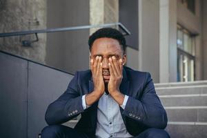 hombre de negocios africano sentado frustrado en las escaleras deprimido por los resultados de su trabajo foto