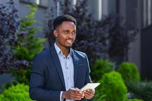 joven hombre de negocios afroamericano en traje de negocios formal de pie trabajando con tableta foto