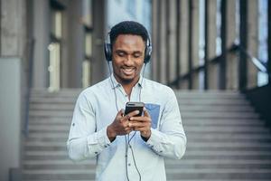 young african student listening to music from smartphone using big headphones photo