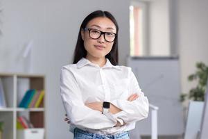 retrato de un joven asiático negocio mujer, un trabajador en el oficina con cruzado foto