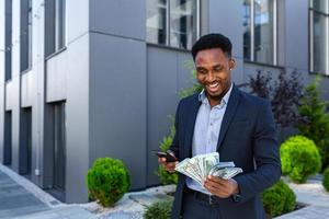 africano americano empresario en pie en calle moderno edificio espectáculo ganancias victorioso foto