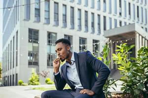 hombre de negocios afroamericano fumando cannabis al aire libre sentado en un banco del parque de la ciudad foto